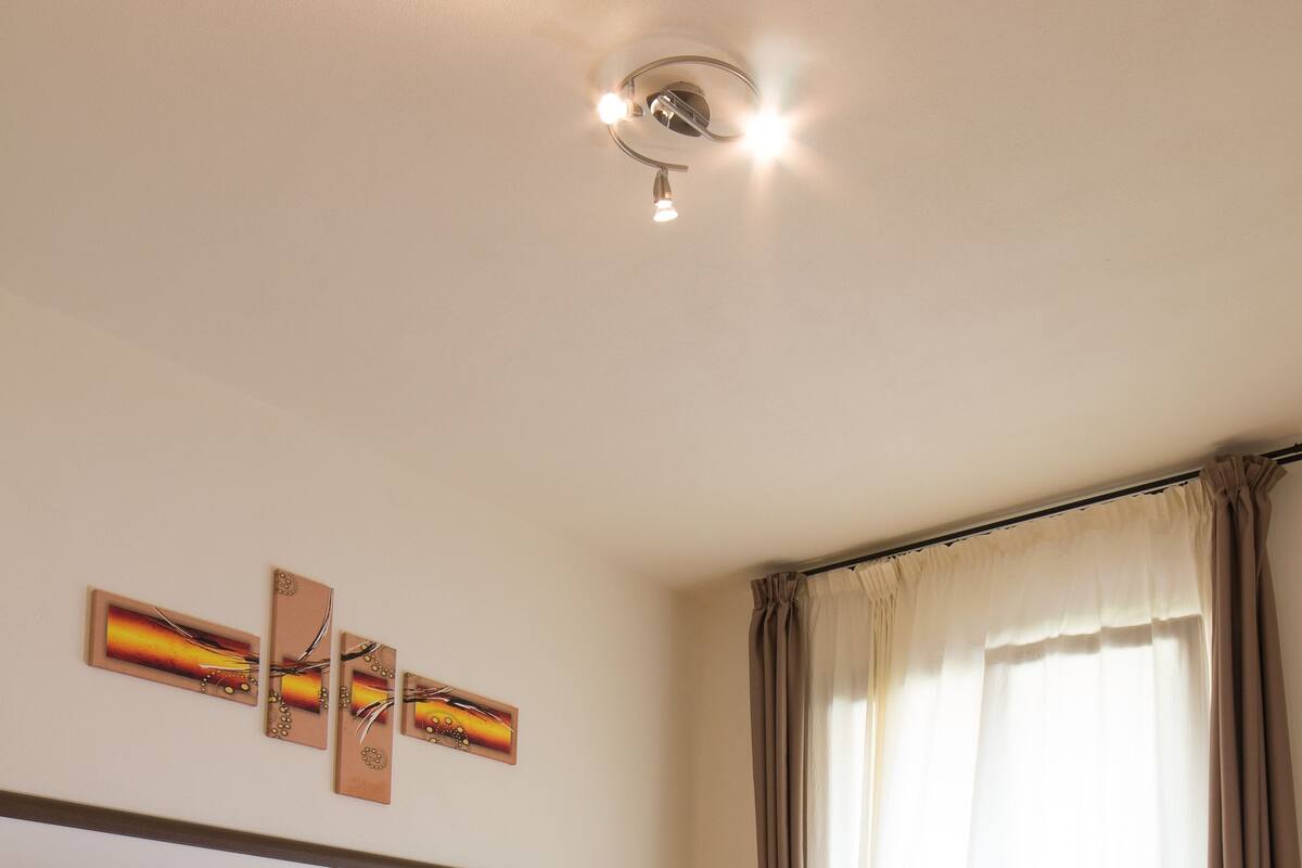 A hotel room with two beds, a large window with curtains, a ceiling light, and wall art.