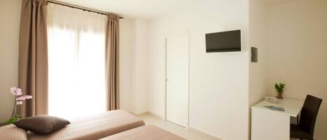 Une chambre d’hôtel avec deux lits, un bureau avec une chaise, une télévision et une petite plante.