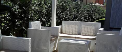 En udendørs patio med hvide fletmøbler, herunder sofaer og et sofabord, under en hvid pergola.