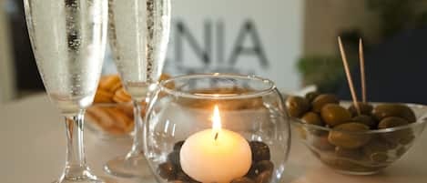 A table setting with two glasses of water, a lit candle in a glass bowl with pebbles, and a bowl of olives.