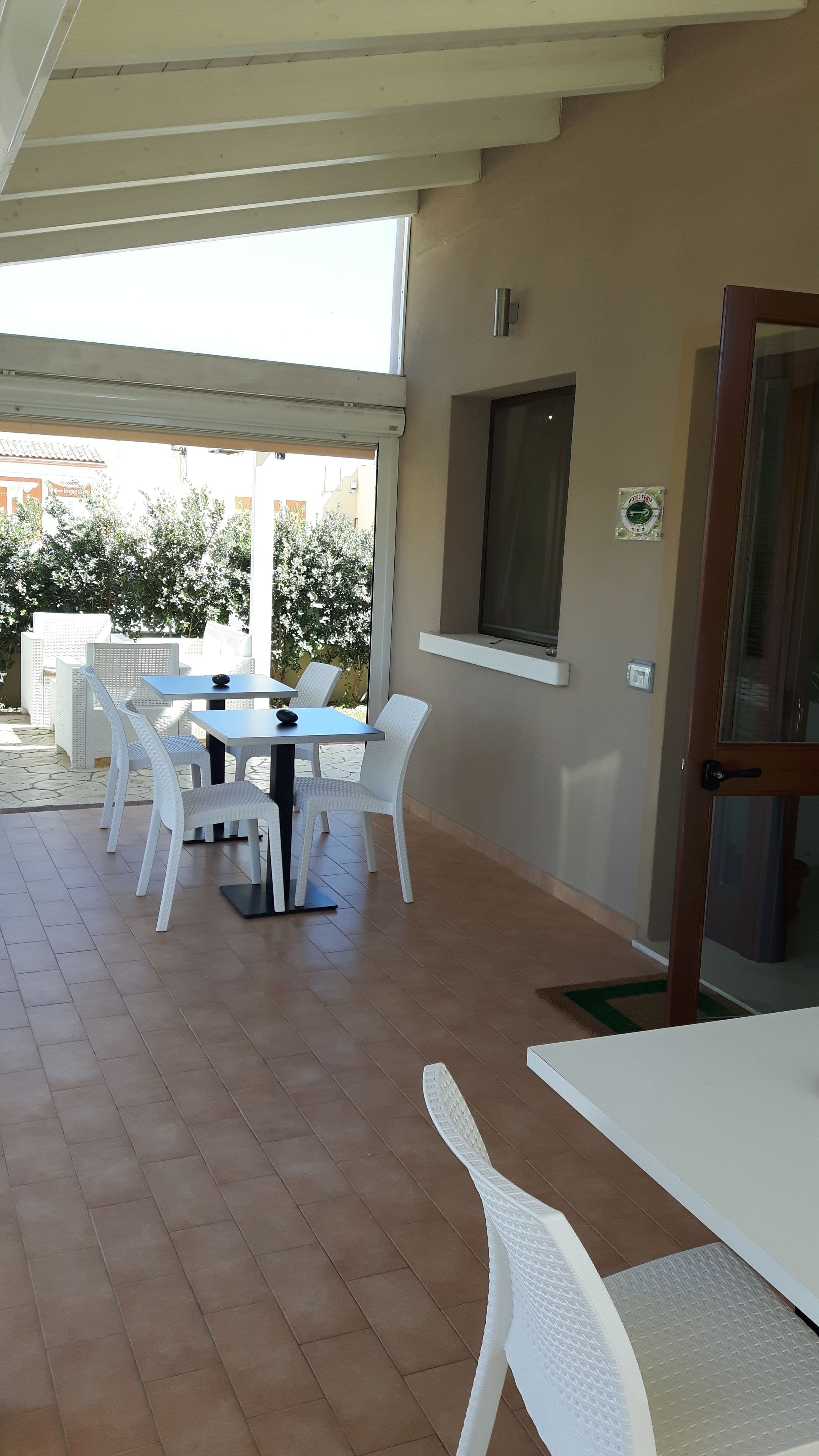 A covered patio area with white wicker furniture, a tiled floor, and a window with a view of the outside.