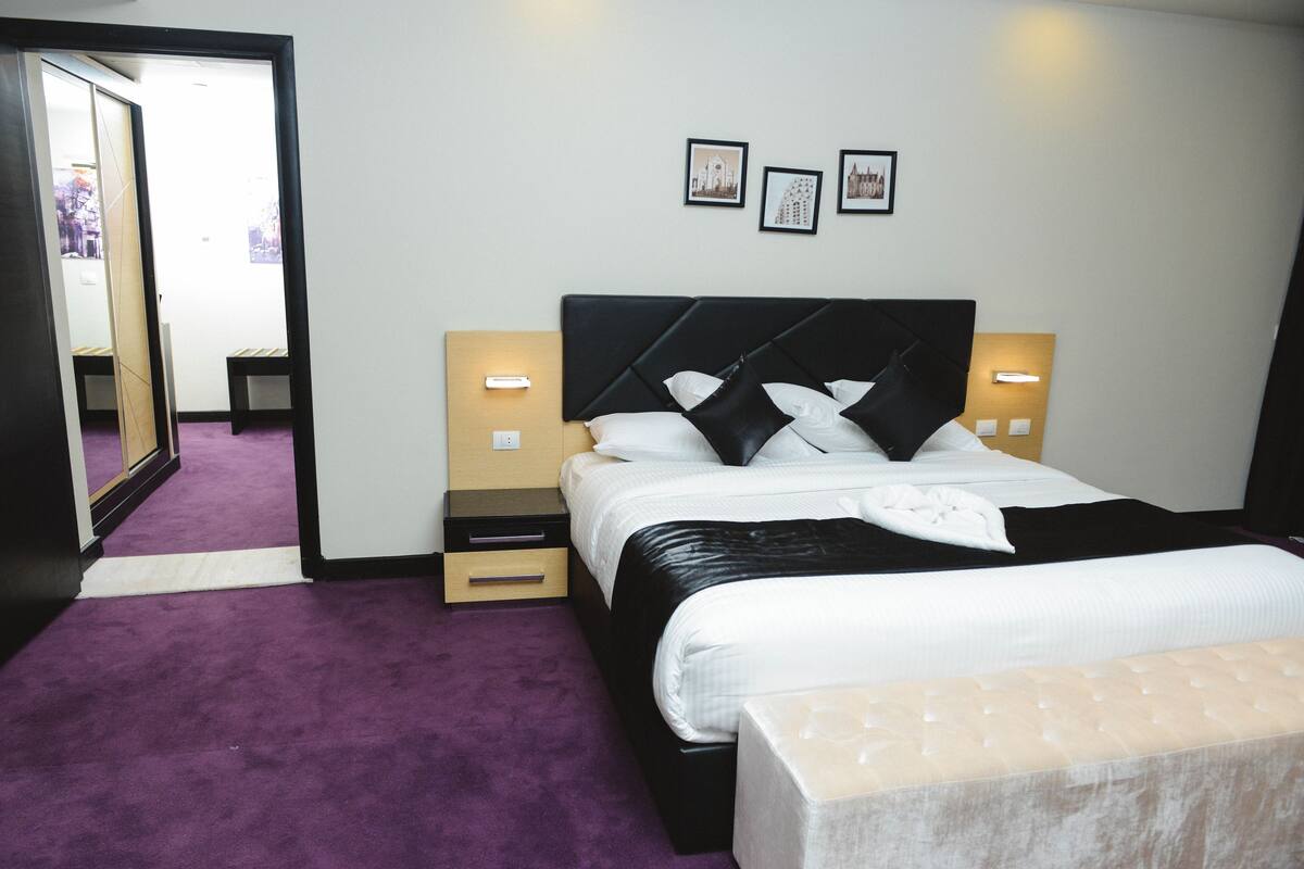 Una habitación de hotel con una cama, mesitas de noche, un espejo y cuadros en la pared.