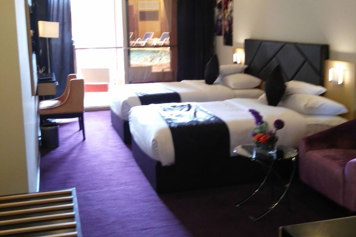 Habitación de hotel con dos camas, un escritorio, una silla, un televisor y una ventana con cortinas.