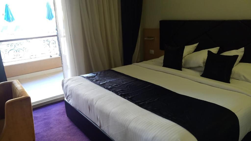 A hotel room with a bed, a chair, a window with curtains, and a view of the outdoors.