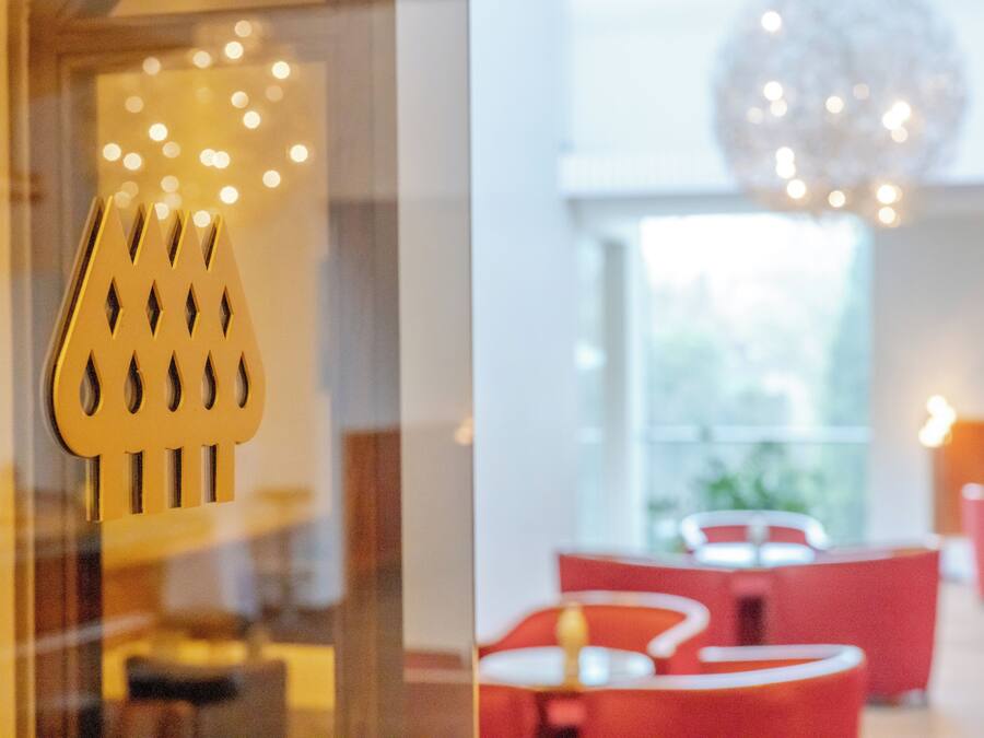 Un interior moderno con un panel de vidrio que incluye un elemento metálico decorativo, asientos rojos y una gran lámpara esférica.