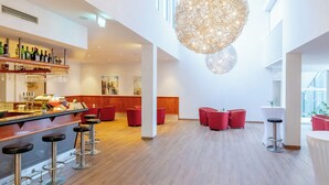 A modern bar area with a wooden floor, red bar stools, and a variety of bottles and glasses on the shelves. - Parkhotel Styria (Steyr)