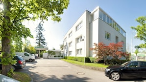 A modern hotel with a white facade, large windows, and a parking area with cars. - Parkhotel Styria (Steyr)