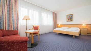 Una habitación de hotel con una cama, una silla, una mesita pequeña y una mesita de noche con una lámpara.