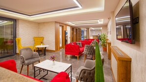 A modern lounge area with red and grey upholstered seating, a marble coffee table, and a flat-screen TV mounted on the wall. - Sim Hotel (Istanbul)