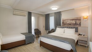 A hotel room with two single beds, a sitting area with a chair, a desk with a lamp, and a wall-mounted air conditioner. - Sim Hotel (Istanbul)