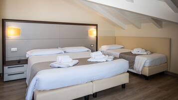 A hotel room with a large bed, two smaller beds, a bedside table, and a nightstand.
