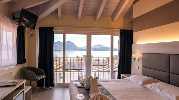 A hotel room with a bed, a desk, a chair, and a balcony with a view of the sea and mountains. - Hotel Rosa (Baveno)