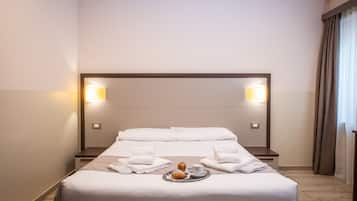 A neatly made bed with white linens, a tray with croissants and a cup of coffee, and two wall-mounted lamps.