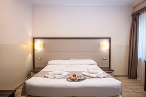 Una cama impecablemente tendida con sábanas blancas, una bandeja con croissants y una taza de café, y dos lámparas fijadas a la pared.