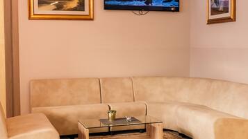 Una sala de estar con un sofá color beige, una mesa de centro de cristal y un televisor montado en la pared que muestra una escena de atardecer.