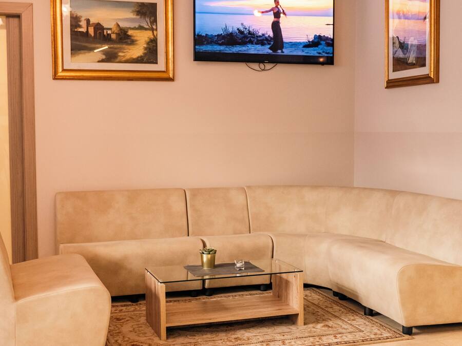 Una sala de estar con un sofá color beige, una mesa de centro de cristal y un televisor montado en la pared que muestra una escena de atardecer.