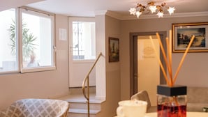 A hotel room with a sofa, a table with a cup and a remote control, a door with a sign, and a staircase. - Hotel Rosa (Baveno)