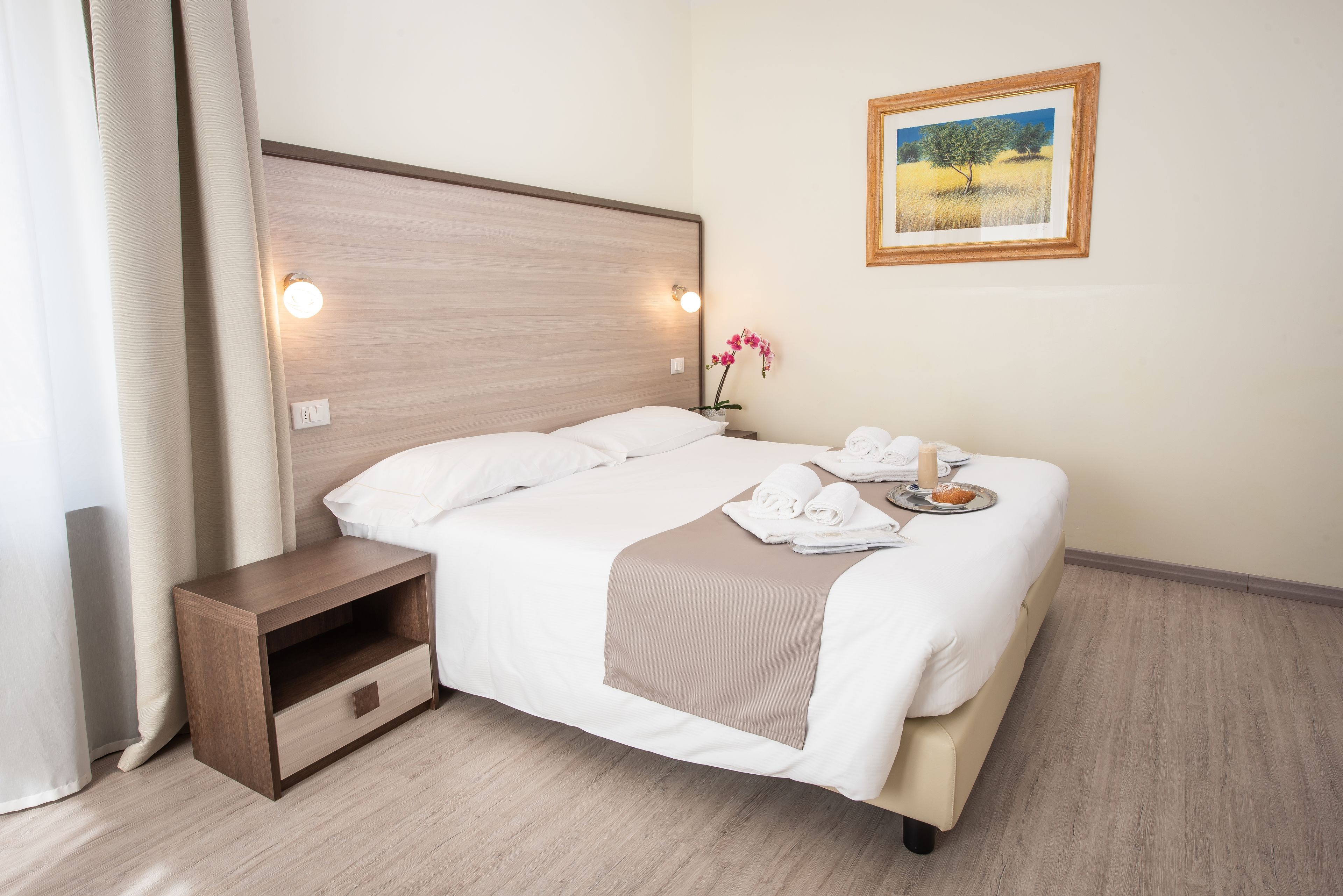 Un lit bien fait, avec du linge de lit blanc, un plaid marron et un plateau contenant des serviettes et une bougie.