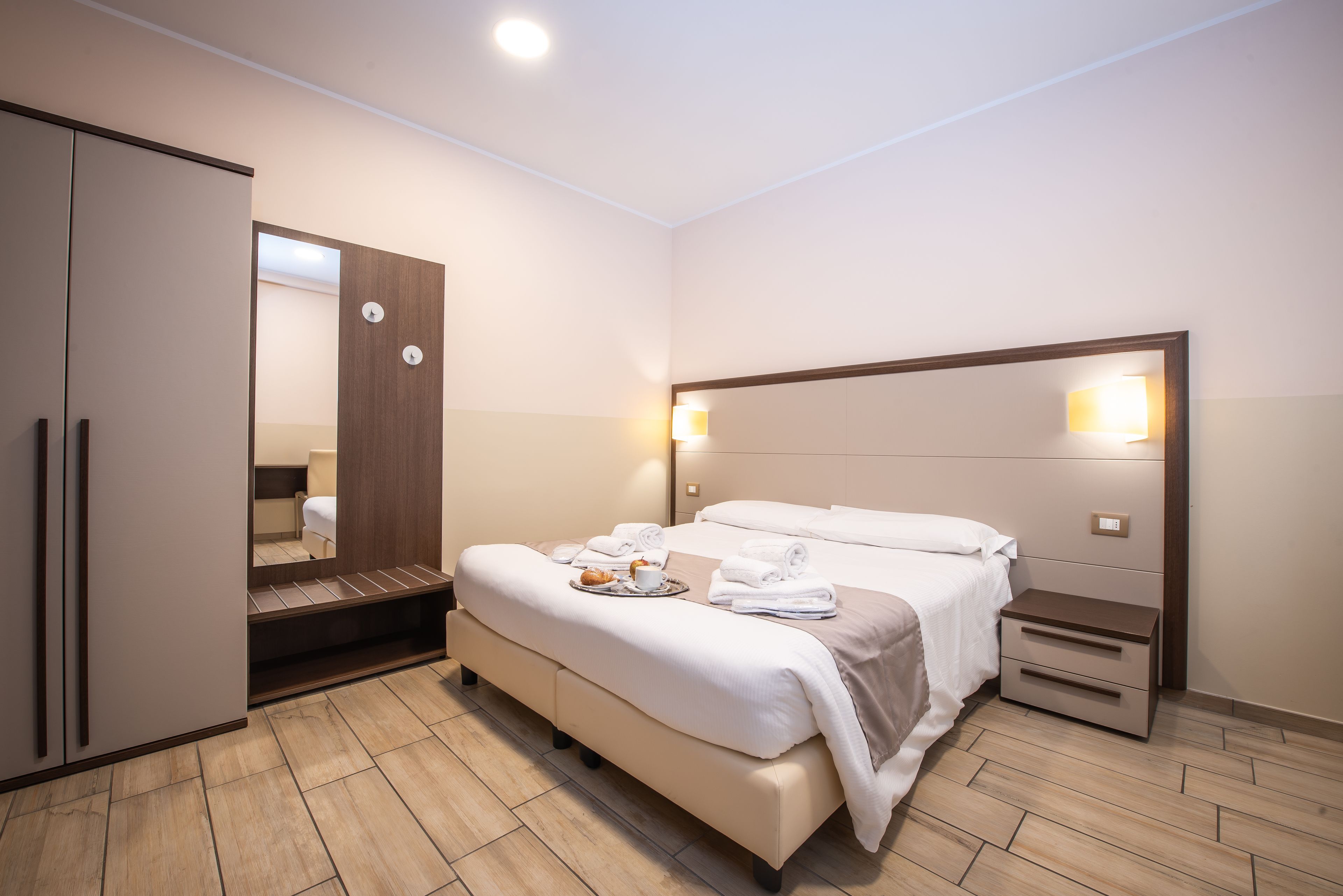 Habitación de hotel con una cama grande, un armario, una mesita de noche y un espejo.