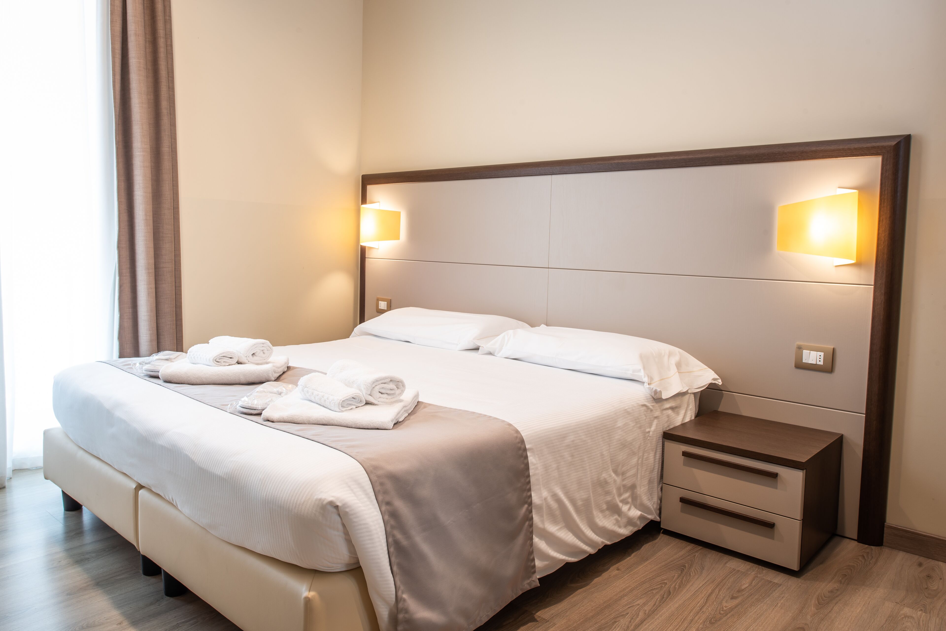 Een opgemaakt bed met een hoofdbord, nachtkastjes en een lamp.