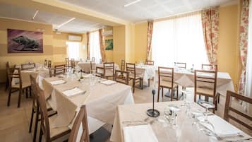 Restaurante com várias mesas preparadas para refeições, apresentando teto com padrão de grade e cortinas florais.