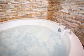 A bathtub with a stone mosaic wall.