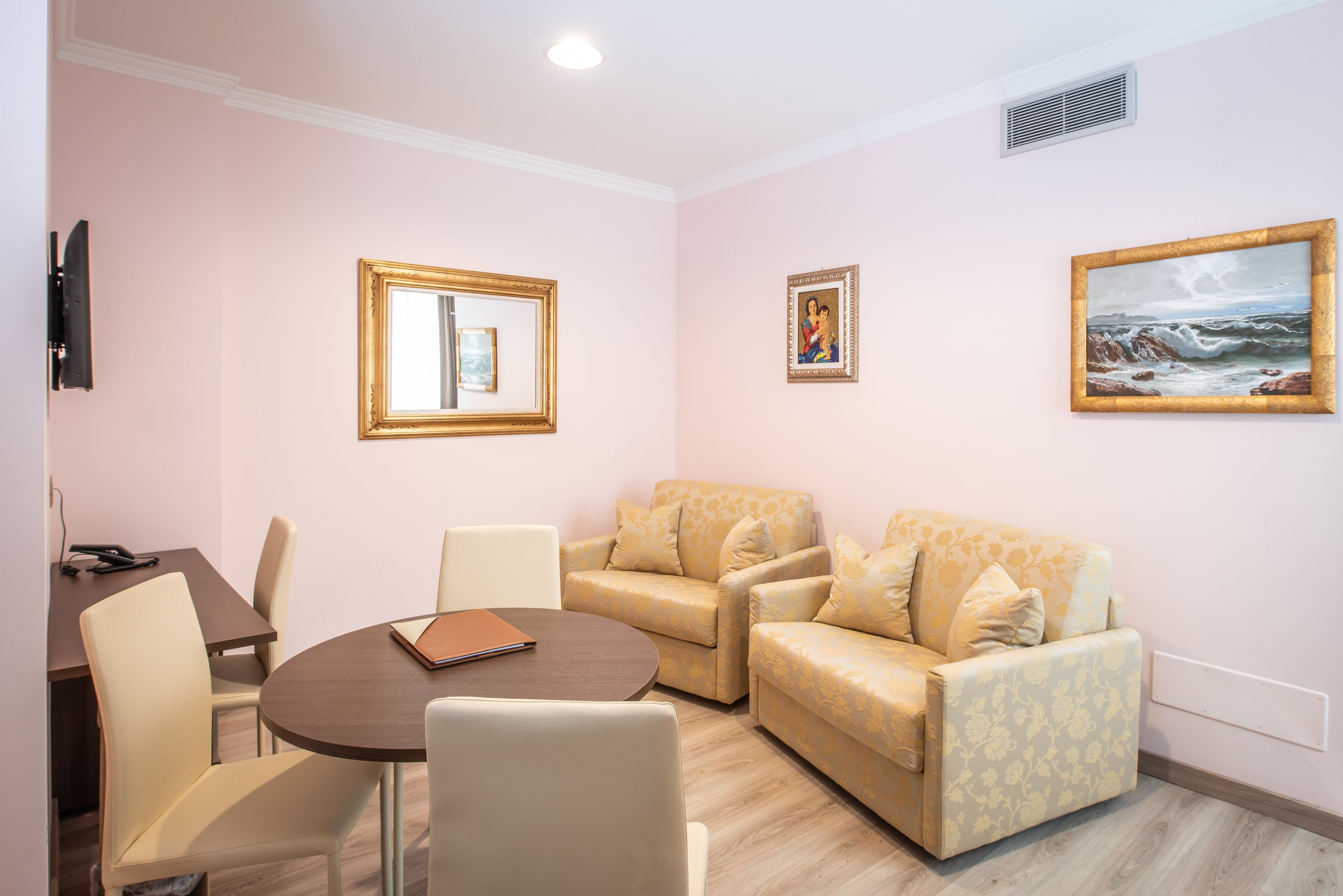 A room with a round table, two sofas, a TV, and framed pictures on the wall.