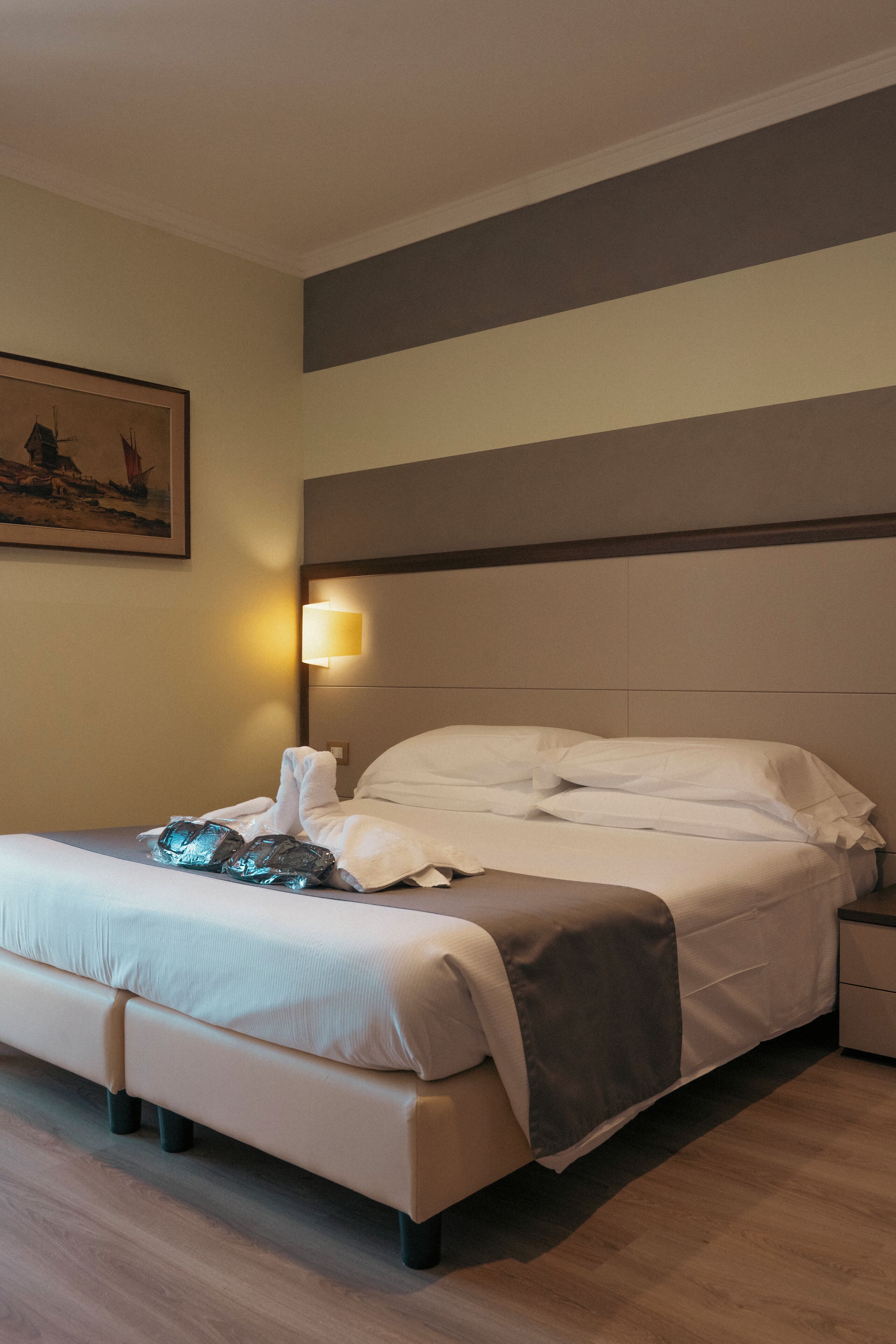 A hotel room with a bed, a bedside lamp, a nightstand, and a painting on the wall.