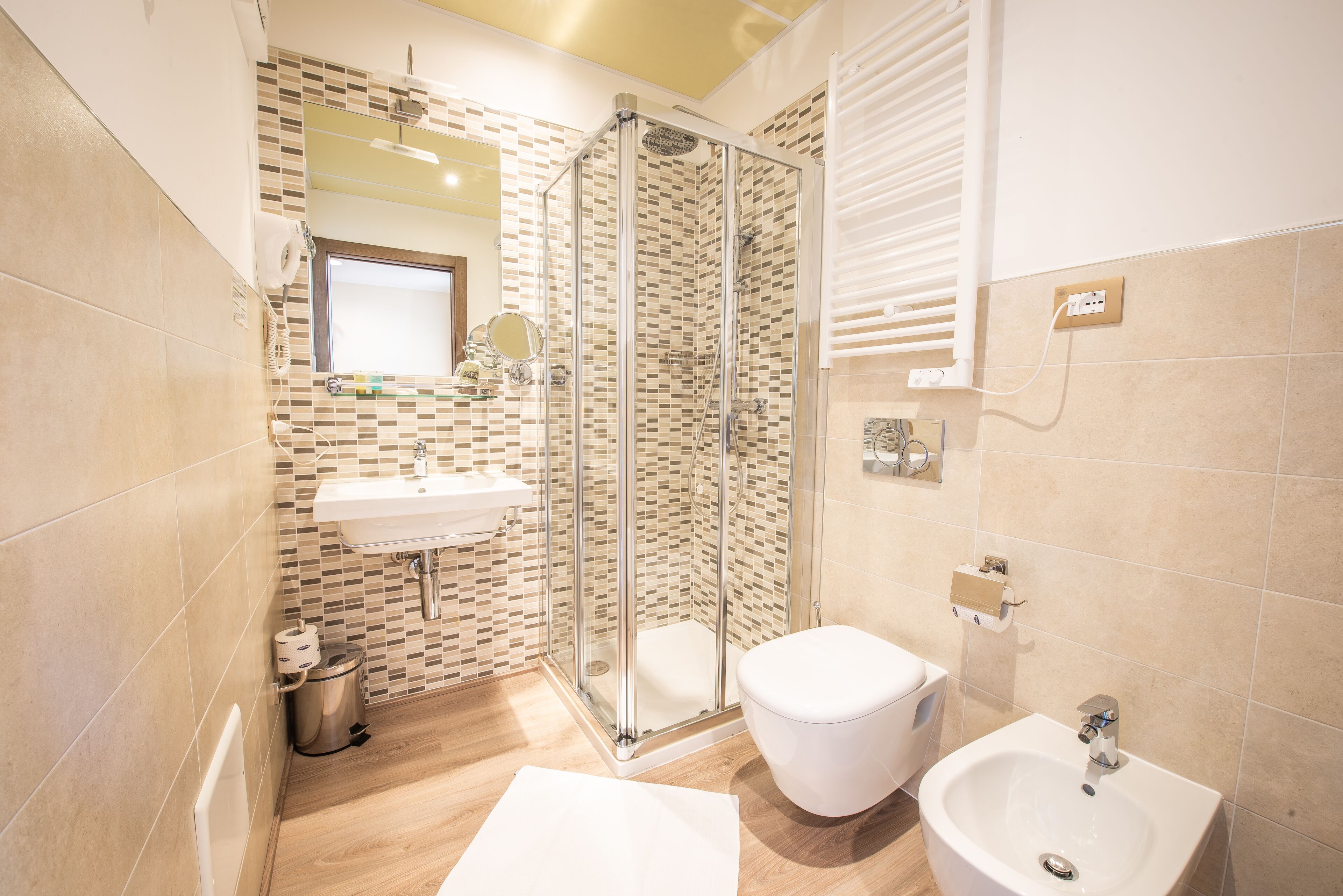 A bathroom with a glass shower enclosure, a sink, a toilet, and a bidet.