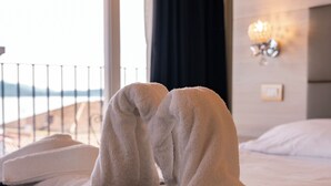 A bed with a white towel draped over it, a window with a view of the outdoors, and a wall-mounted light fixture. - Hotel Rosa (Baveno)