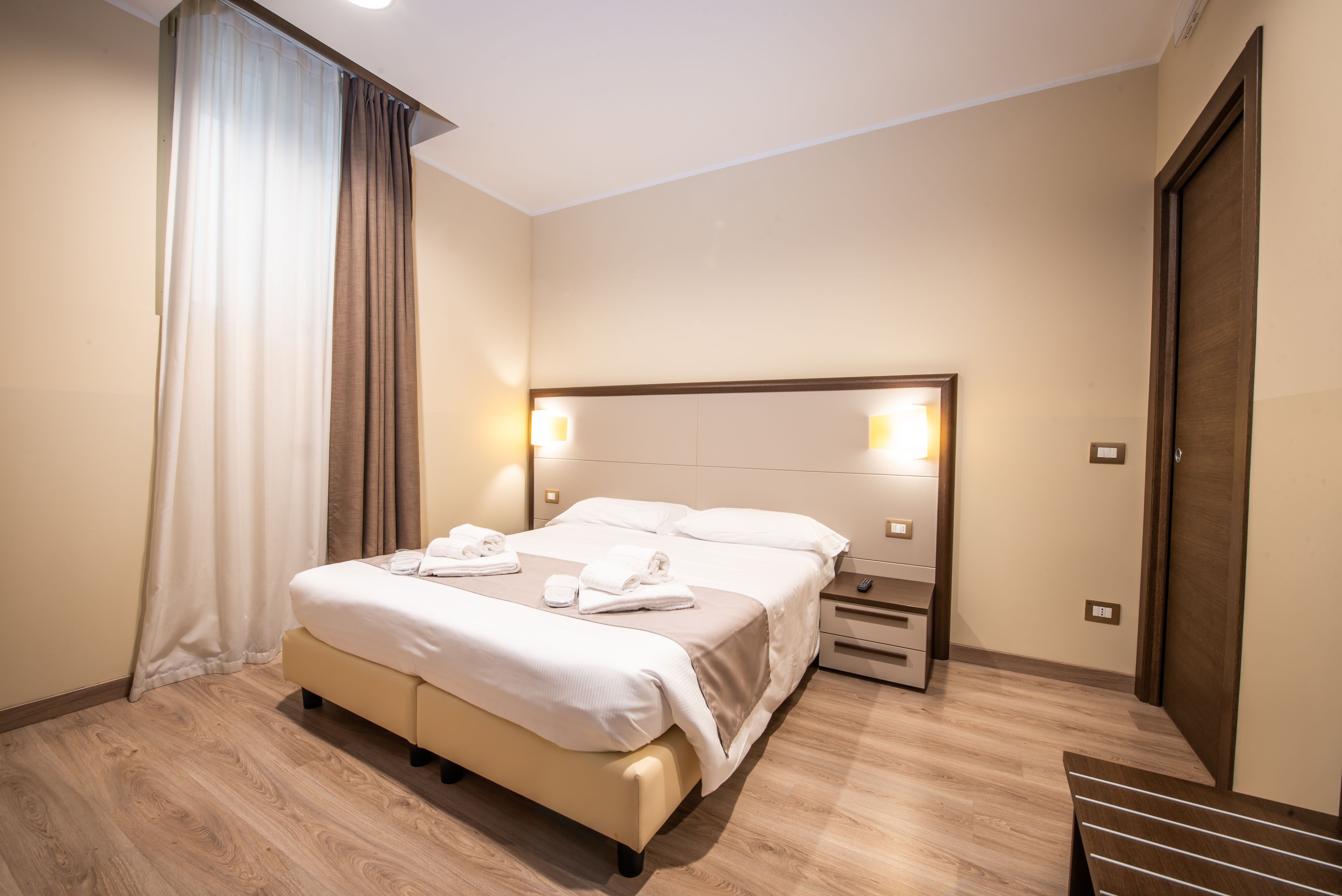Una camera d'albergo con un letto grande, comodini, pavimento in legno e una porta.