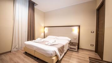 Una camera d'albergo con un letto grande, comodini, pavimento in legno e una porta.