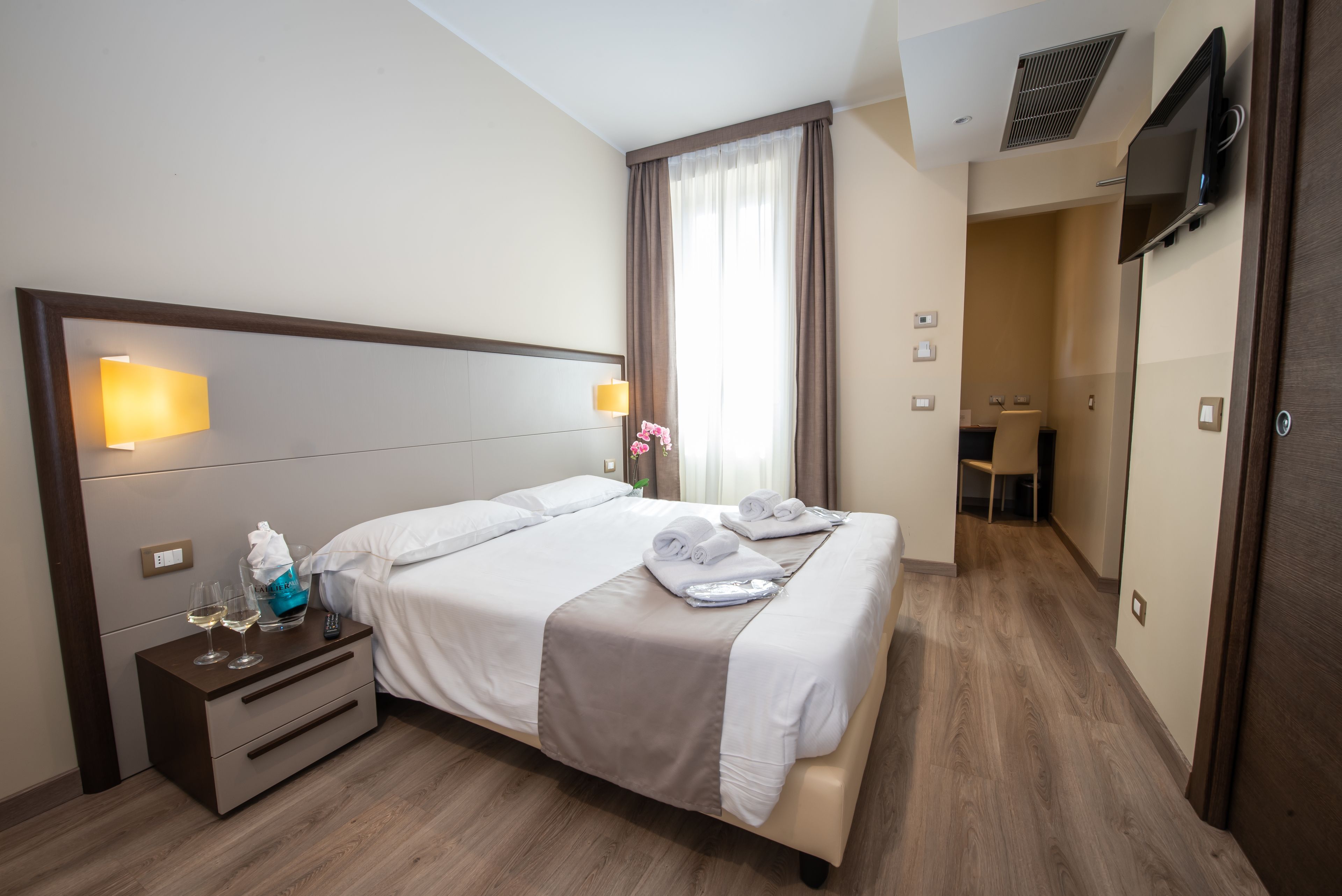 Una habitación de hotel con cama, mesita de noche y televisor montado en la pared.