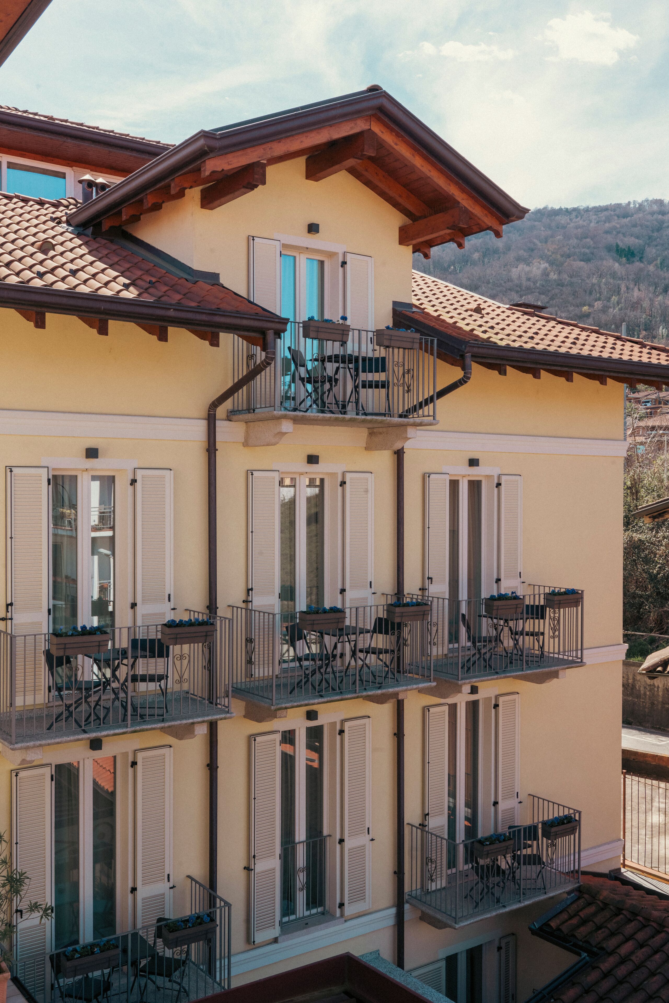 Un immeuble à plusieurs étages doté de balcons, de fenêtres avec volets et de mobilier d’extérieur.