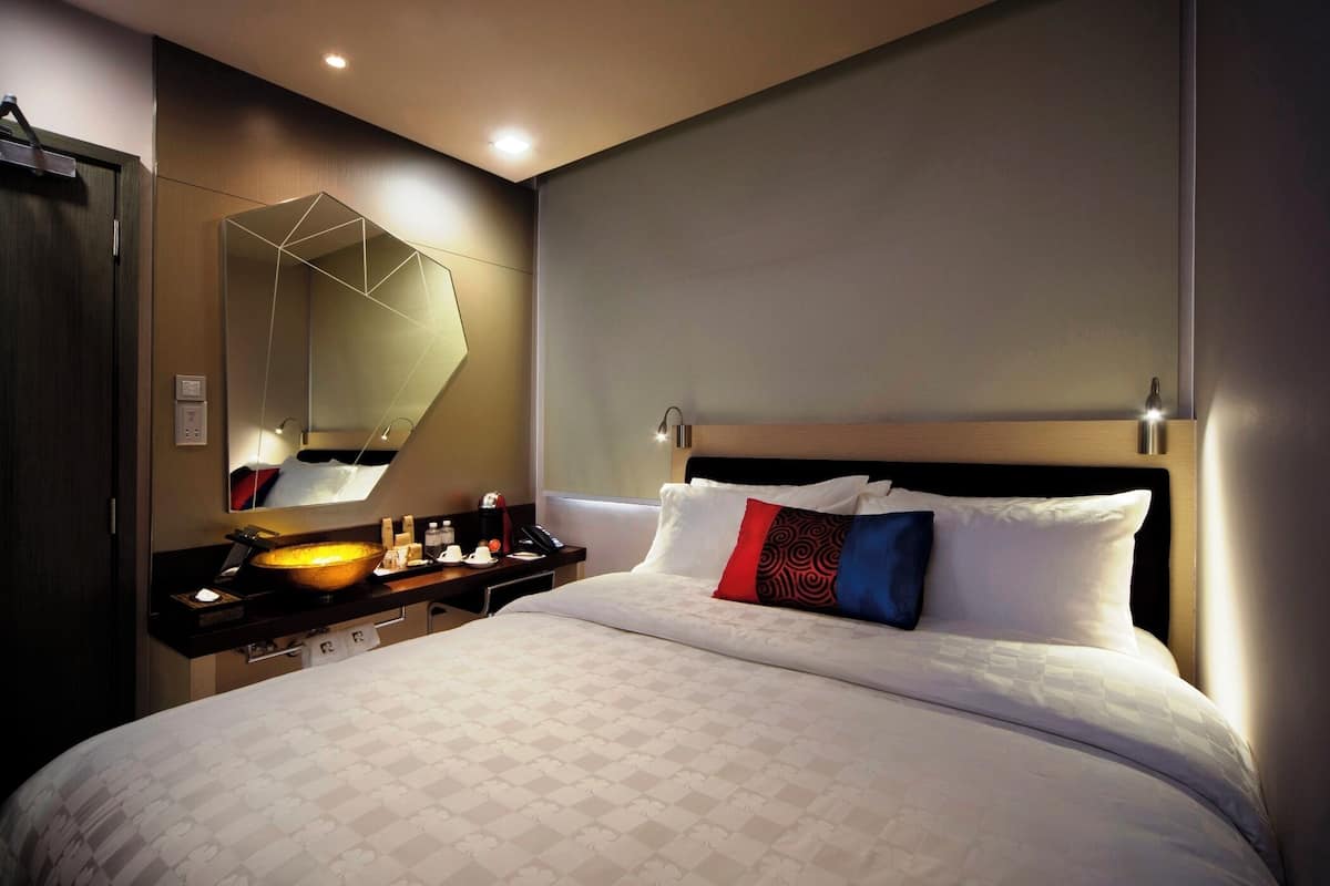 A hotel room with a large bed, a bedside table with a mirror, and a modern bathroom with a large mirror.