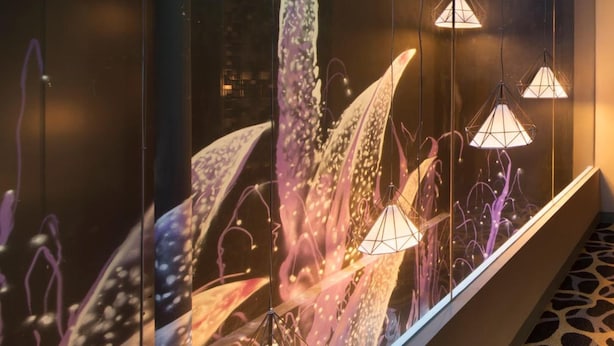 Un pasillo con una pared de vidrio que muestra una llamativa instalación de arte abstracto.