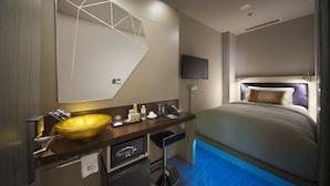 Una habitación de hotel moderna con un espejo grande, un lavamanos de estilo cuenco dorado, un televisor de pantalla plana, una cama con cabecero y un escritorio pequeño con cafetera.
