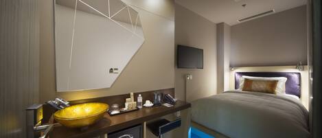 Una habitación de hotel moderna con un espejo grande, un lavamanos de estilo cuenco dorado, un televisor de pantalla plana, una cama con cabecero y un escritorio pequeño con cafetera.