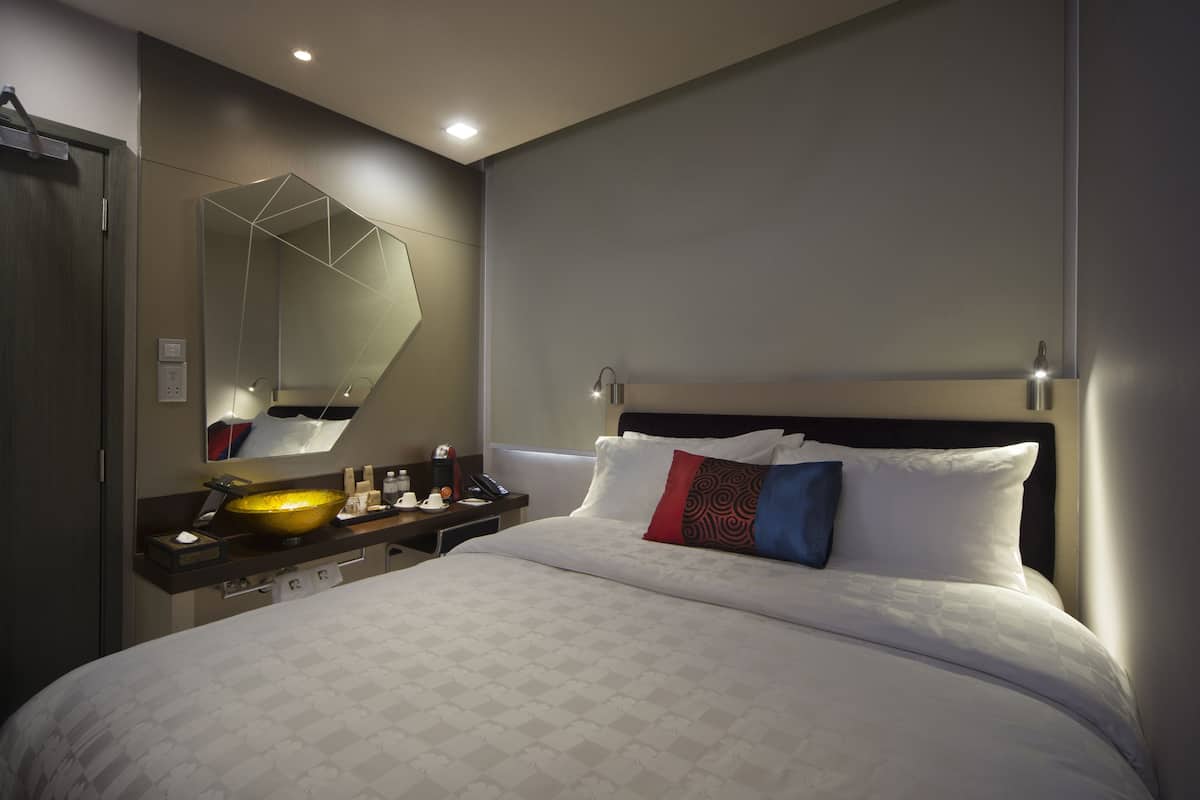 A modern hotel room with a large bed, a bedside table with a bowl sink, and a large mirror.