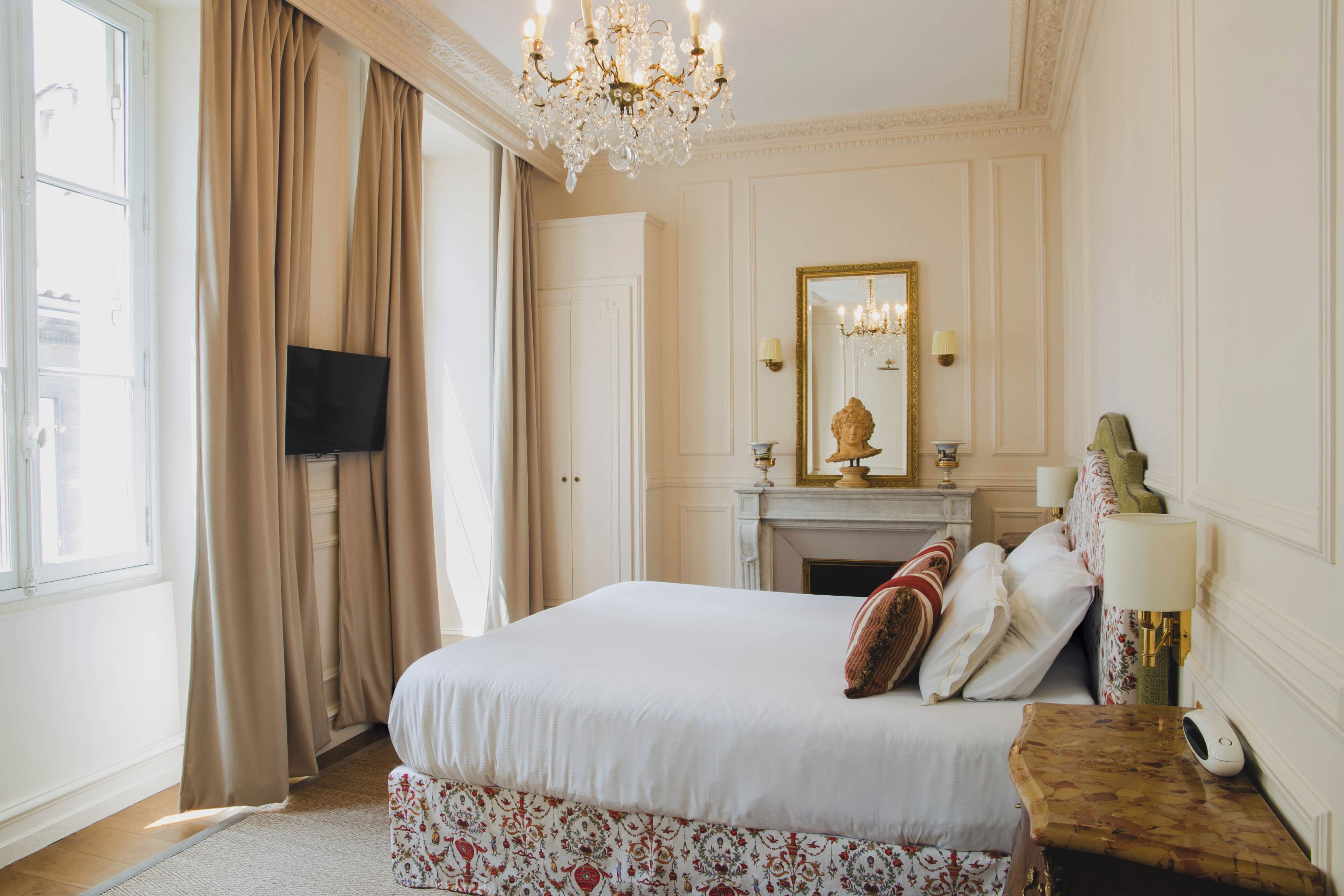A hotel room with a large bed, a fireplace, a mirror, and a television on the wall.