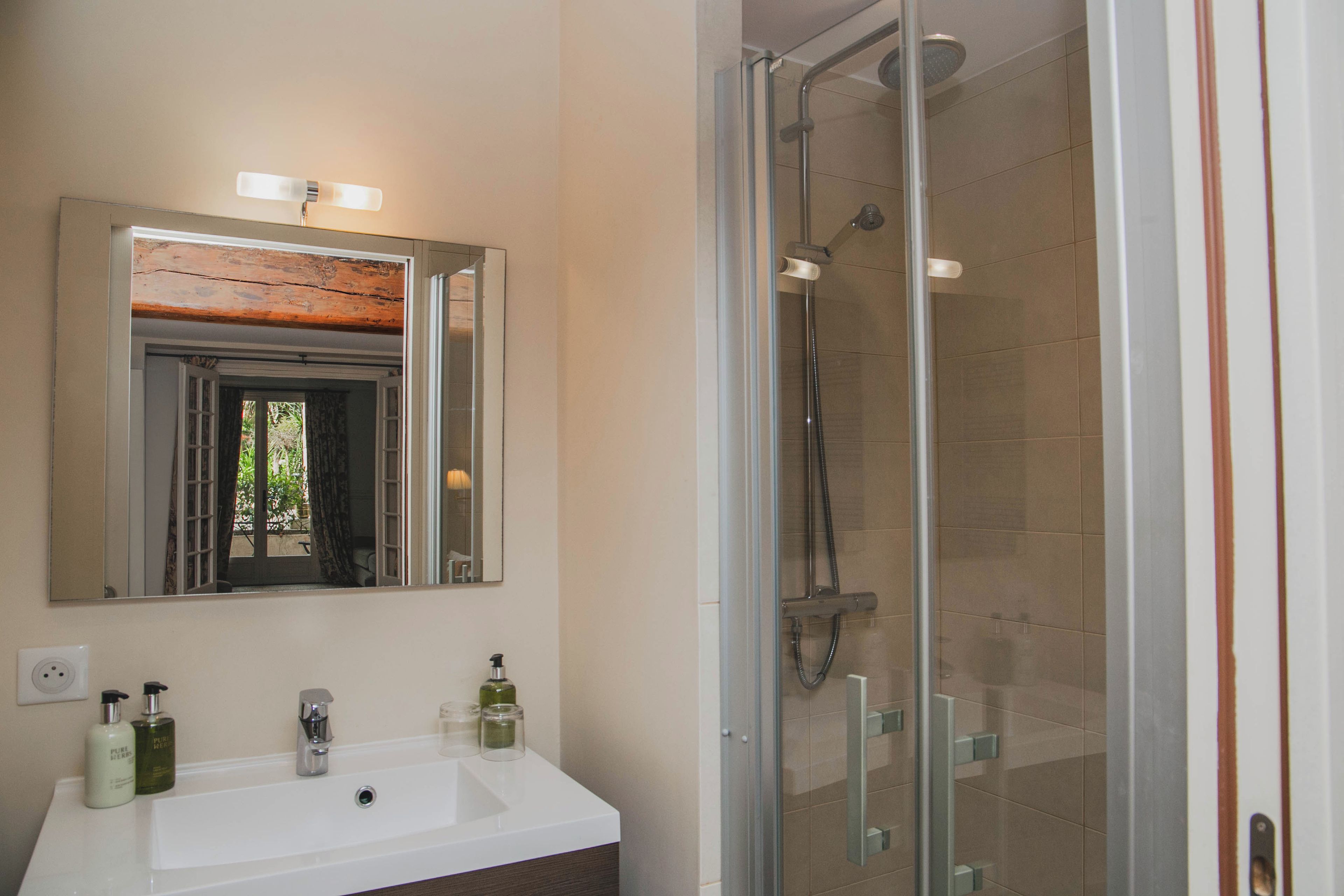 A bathroom with a white sink, two bottles of liquid soap, a mirror, and a glass-enclosed shower area.