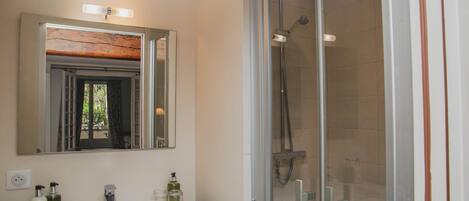 A bathroom with a white sink, two bottles of liquid soap, a mirror, and a glass-enclosed shower area.