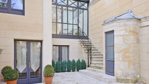 A courtyard with a stone staircase, a door with curtains, and potted plants. - Villa Victor Louis (Bordeaux)