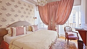 A bedroom with a large bed, a chair, a desk, and a patterned wallpaper. - Villa Victor Louis (Bordeaux)