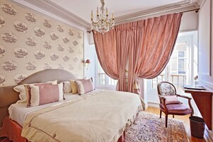 Un dormitorio con una cama grande, una silla, un escritorio y un papel tapiz estampado.