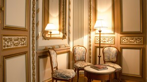 A room with ornate wall paneling, two upholstered chairs, a small round table with a book, and two wall-mounted lamps. - Villa Victor Louis (Bordeaux)