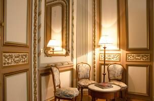 Una stanza con boiserie decorata, due poltrone imbottite, un tavolino rotondo con un libro e due lampade a parete.