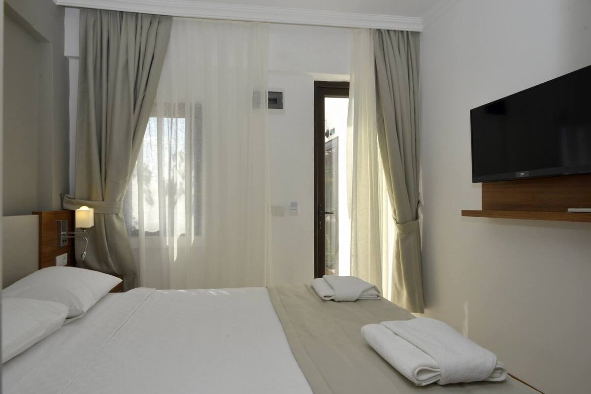 A hotel room with two beds, a TV mounted on the wall, and a window with curtains.