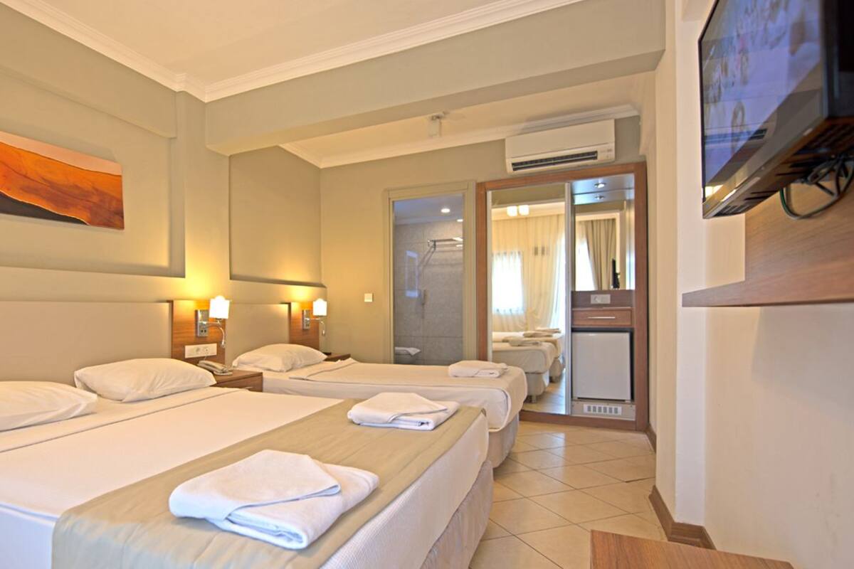 A hotel room with three beds, a TV, a mirror, and a painting on the wall.