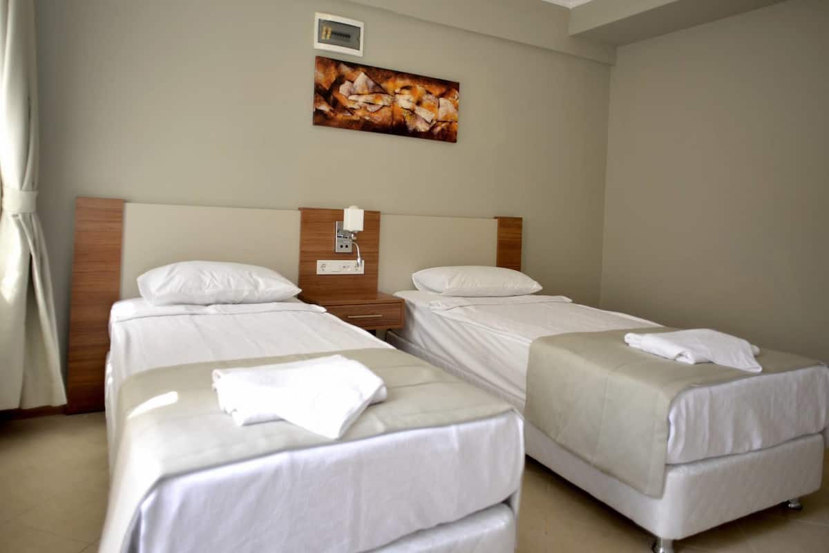 A hotel room with two single beds, a wooden headboard, a nightstand, and a painting on the wall.